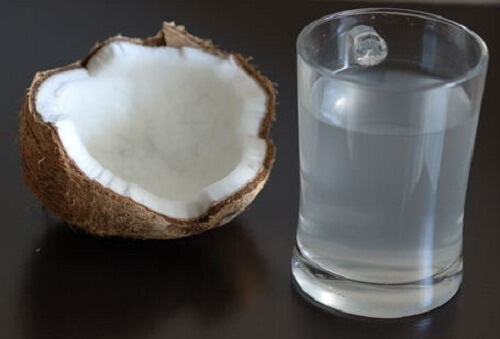 Metade de um coco e um copo com água de coco