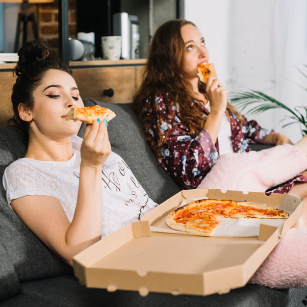 duas meninas comendo uma pizza no sofá