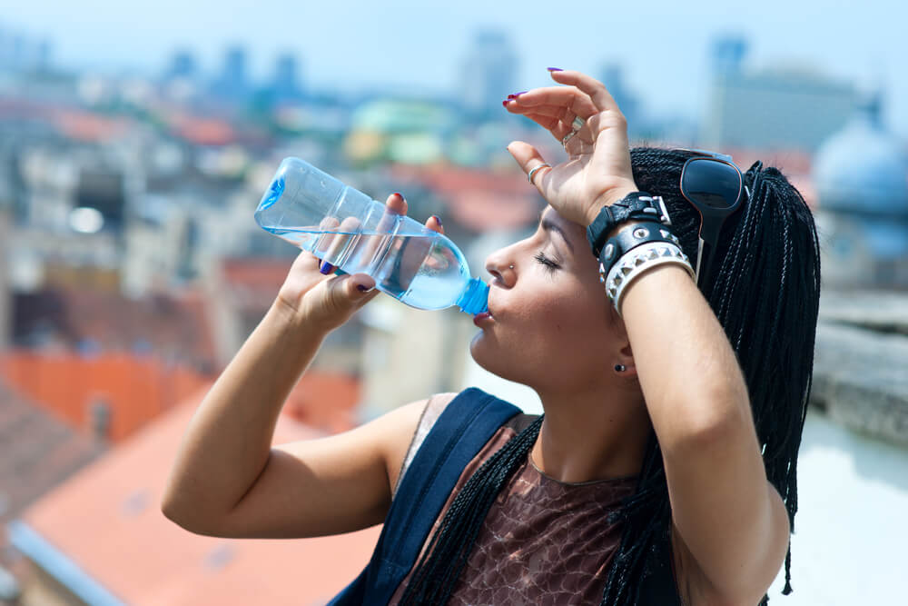 mulher bebendo água em uma garrafinha plástica