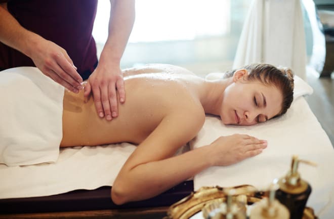 Mulher deitada em mesa de spa recebendo massagem modeladora de profissional