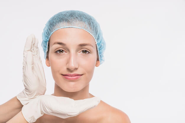 mãos de médico com luva medindo o rosto de uma paciente de touca