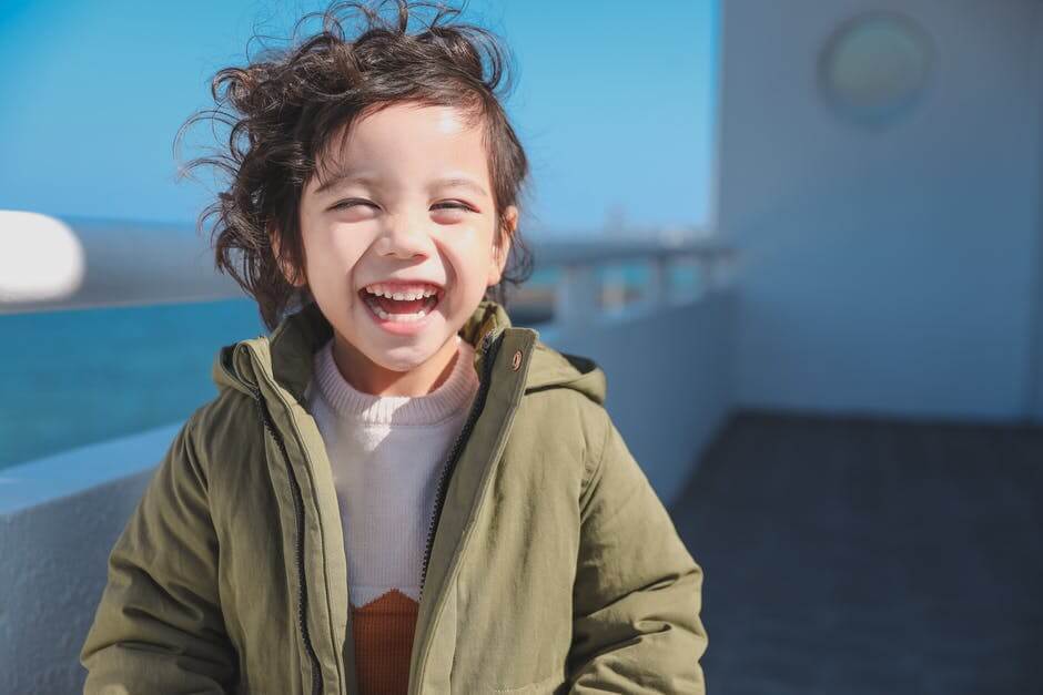 criança de blusa verde com os cabelos ao vento sorrindo no sol
