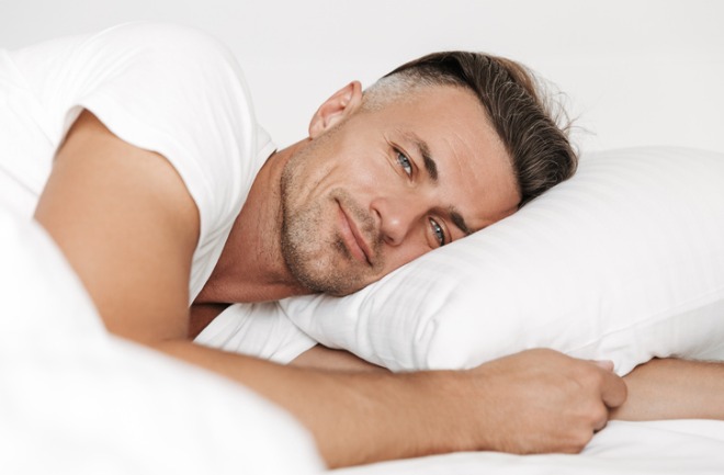homem posando para foto deitado em cama com lençóis brancos após definir a mandíbula