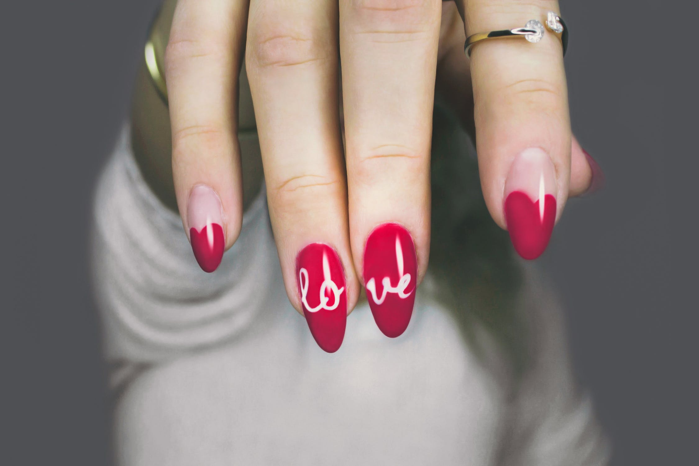 Mão com unha pintada de vermelho e desenhada com a palavra ''love'' nos dois dedos do meio.