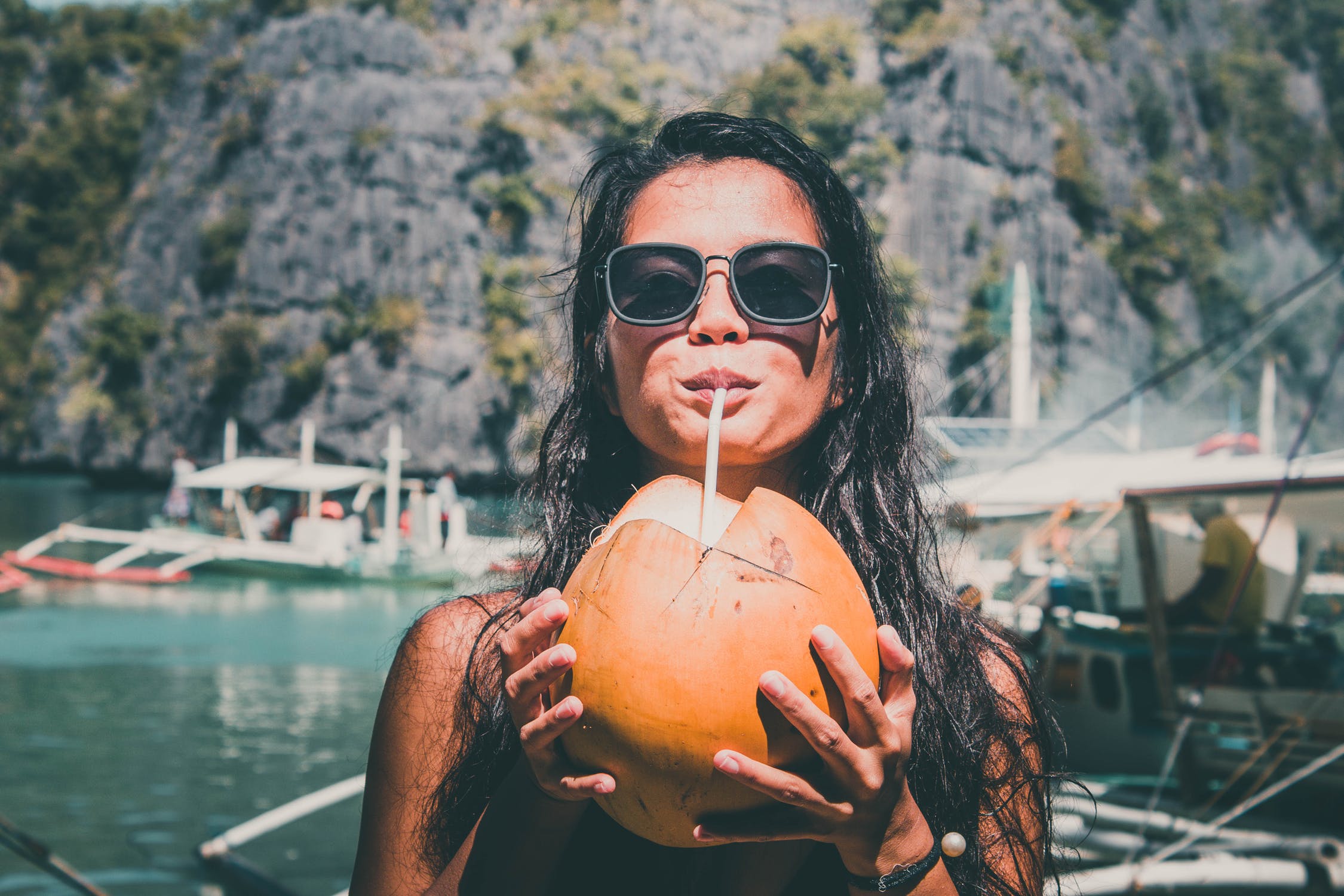 Menina com óculos de sol em barco bebendo água de coco com canudo.