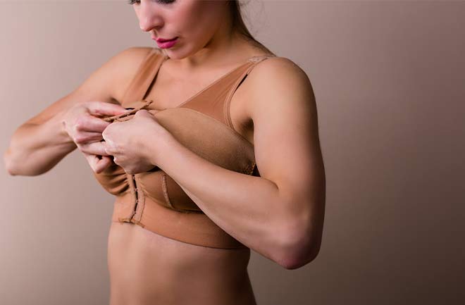 mulher ajustando o sutiâ cirúrgico após cirurgia de mamoplastia