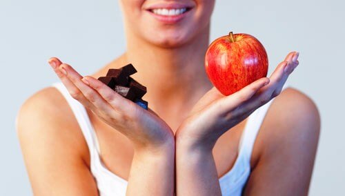 Mulher segurando chocolate em uma mão e uma maçã em outra para manter o peso