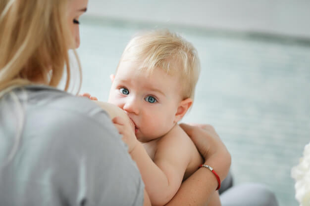 mãe de costas amamentando o bebê loiro de olhos azuis