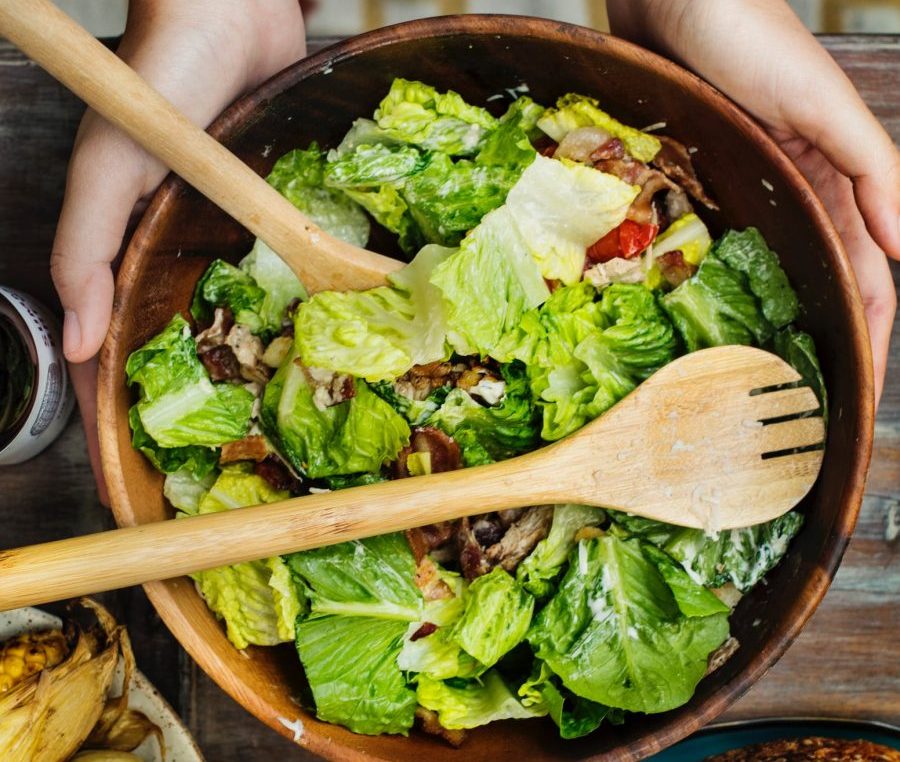 A imagem mostra a mão de uma pessoa segurando um prato de salada verde