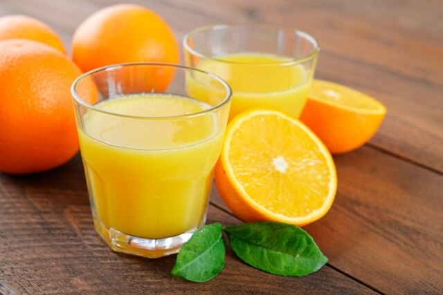 Suco de laranja em um copo e laranjas cortadas sob a mesa