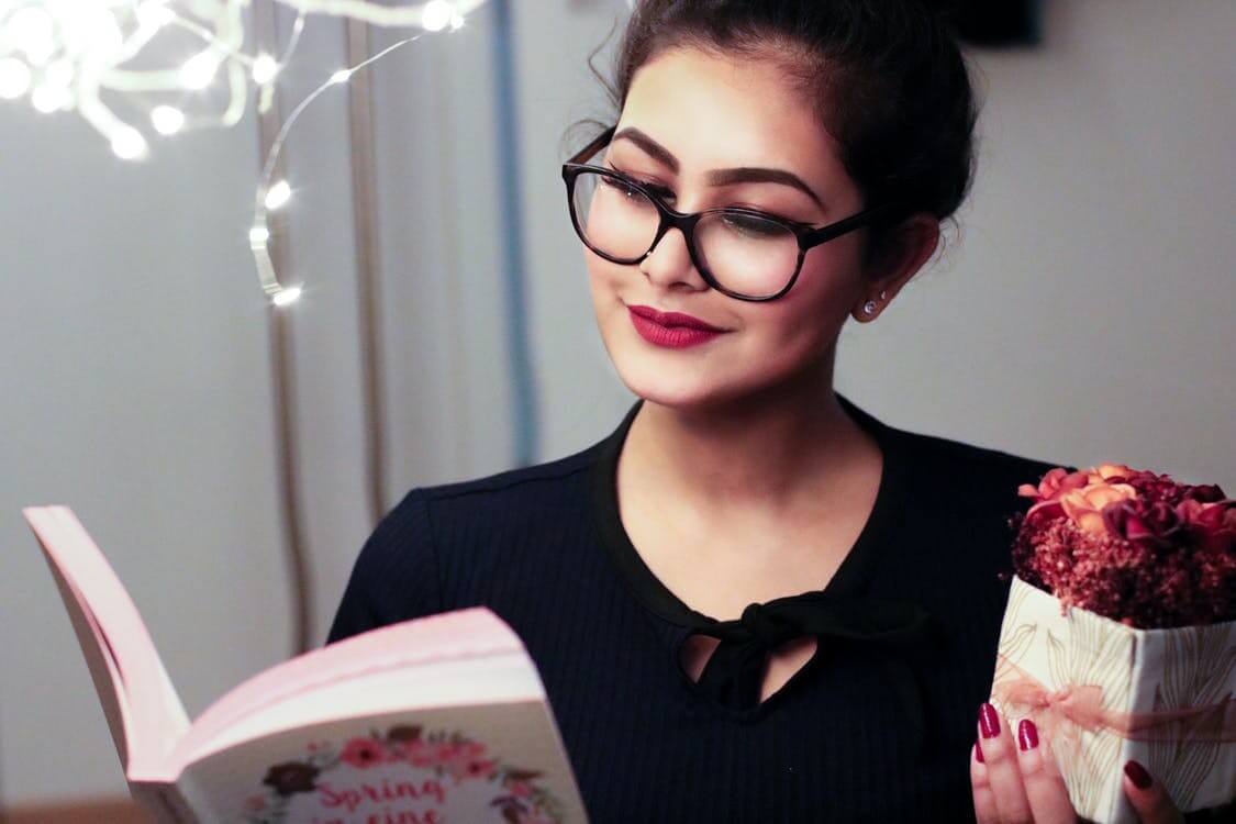 mulher de óculos lendo um livro e sorrindo