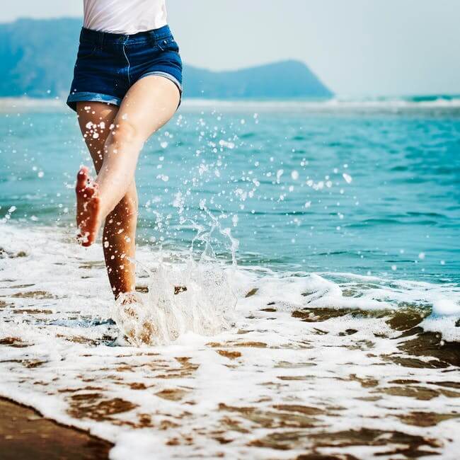 mulher na praia chutando a água feliz